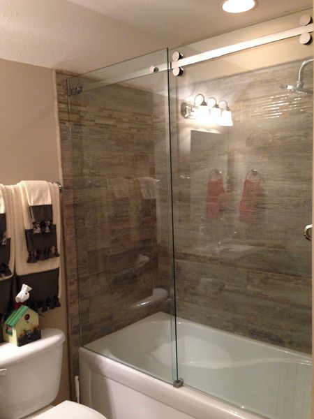 Bathroom with a glass shower door, tiled walls, and a white tub and toilet. Brown and beige color scheme.