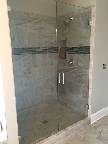 Glass shower enclosure with a door, set in a tiled bathroom. The walls are gray and white, and there is a towel hanging inside.