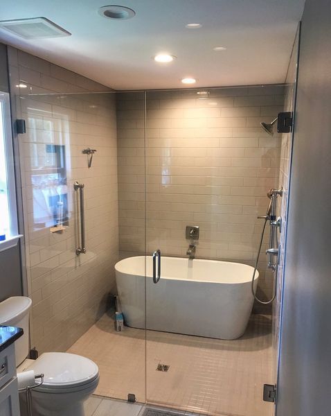 Modern bathroom with a glass-enclosed shower and a freestanding white bathtub. The walls are tiled in a light gray color.