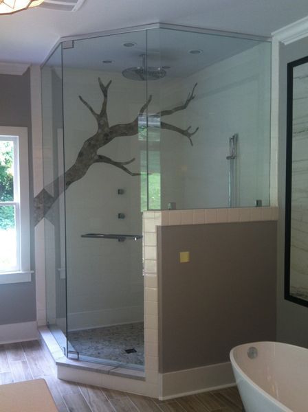 Glass-enclosed shower with a large branch extending across the interior. The shower has gray and white walls, a stone floor, and a tub is visible in the foreground.