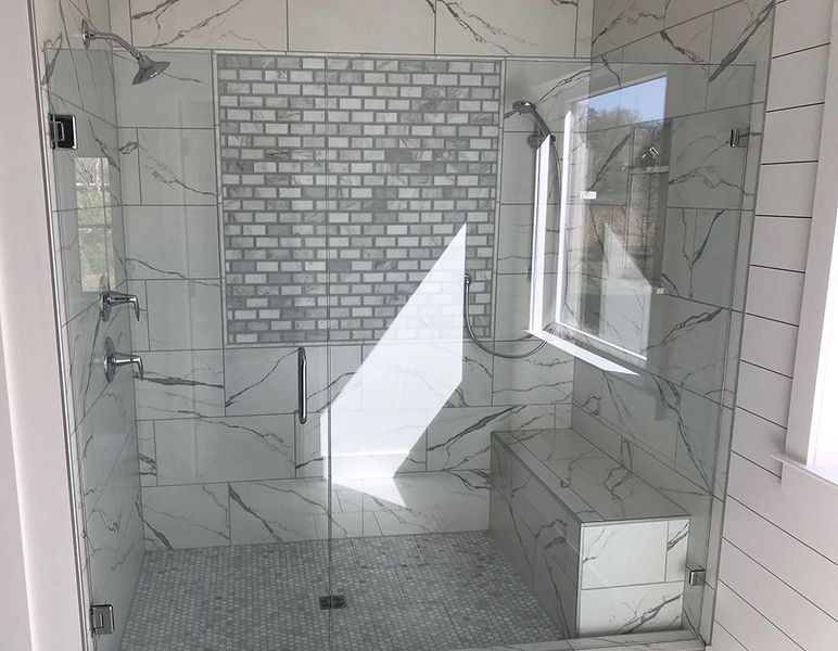 A modern shower with white marble-look tiles, a glass door, and a bench. A window is on the right.