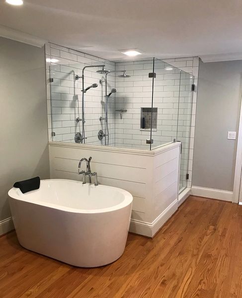 Modern bathroom with a white soaking tub and a glass-enclosed shower with multiple showerheads. Wood floors and white-painted walls.
