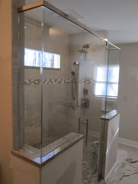 Glass-enclosed shower with neutral-toned tile and granite accents. A window and shower fixtures are visible inside the enclosure.