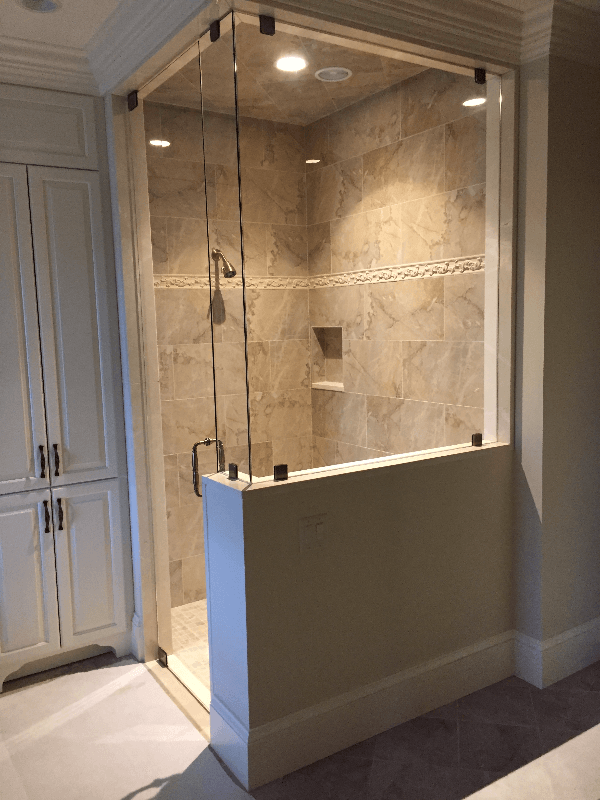 Glass-enclosed shower with a partial wall. The shower features beige tile, a handheld showerhead, and a recessed shelf.