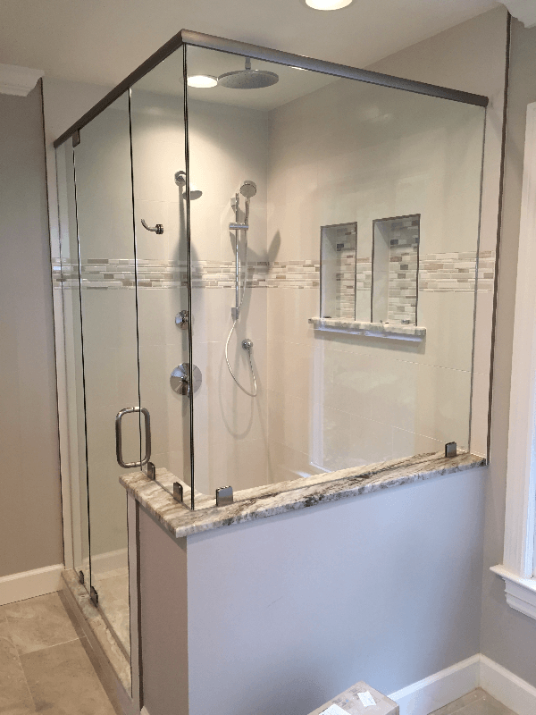 Modern shower with a glass enclosure, gray and white tile, and a granite ledge. The shower includes built-in shelving and various shower fixtures.