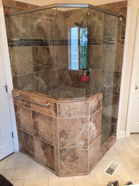 Corner shower stall with brown and tan stone tiles and glass doors. The shower has a built-in seat.