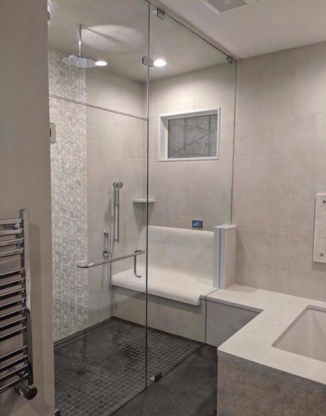 Accessible bathroom with a glass shower enclosure, built-in bench, and grab bar. Light gray tiles and white fixtures create a clean, modern look.
