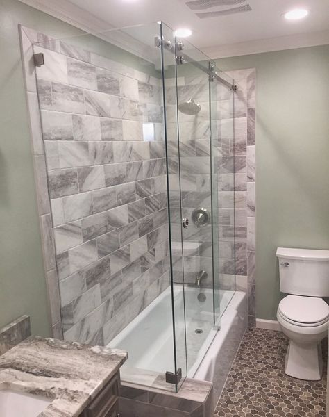 Bathroom with white bathtub and clear glass shower doors, marble-look tile on the shower wall, and a white toilet.