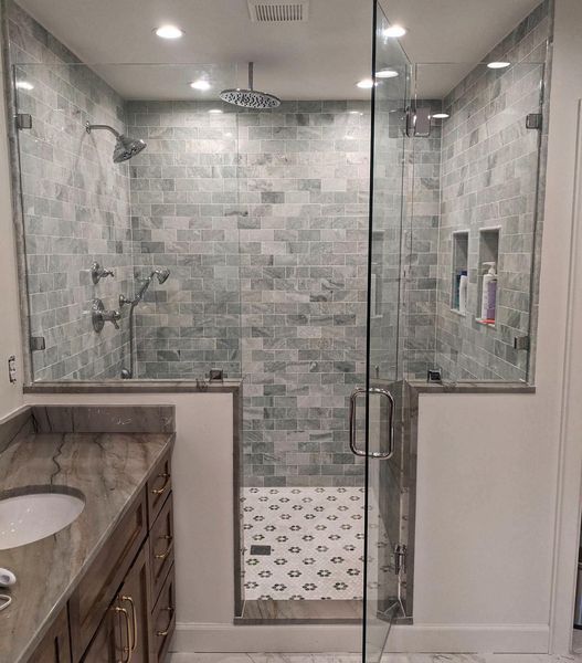 Spacious, modern bathroom with glass-enclosed shower featuring gray-blue tile, multiple shower heads, and built-in shelves.
