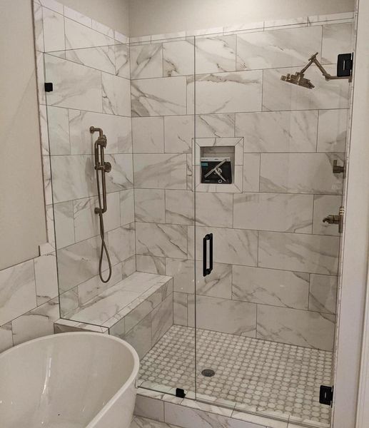 Shower with glass doors, white marble tile, gold-colored shower fixtures, and a built-in bench. An inset shelf is in the wall.