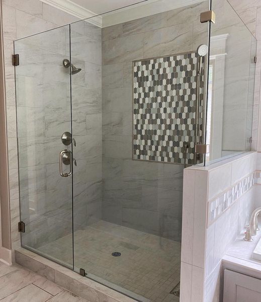 Glass shower enclosure with marble-look tile walls and a decorative tile accent. It has a walk-in entrance and brushed metal fixtures.