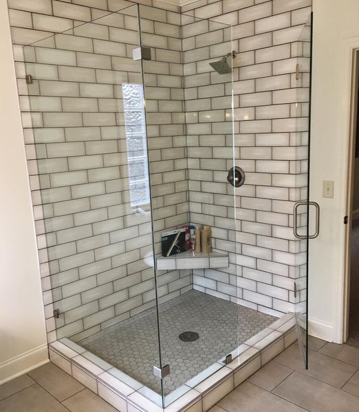 A modern, corner shower with glass doors and white brick-style tile. The shower floor is a mosaic pattern.