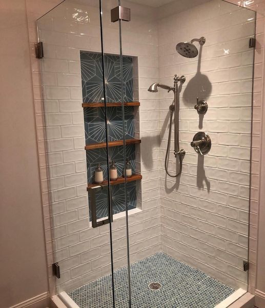 Modern, tiled shower with glass doors. Features blue mosaic floor, white subway tile walls, and a built-in shelf with wooden shelves.