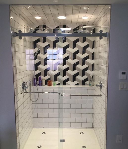 Shower with a geometric tile accent wall, white subway tiles, glass door, and silver hardware.