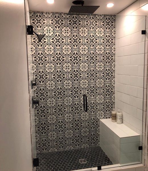 Shower with patterned black and white tile accent wall, glass doors, white bench, and black fixtures.