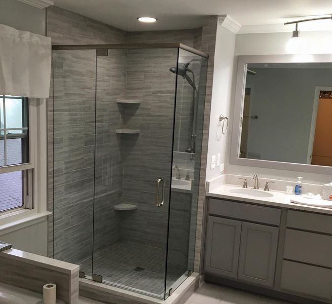 A newly renovated bathroom with a glass shower, grey vanity, and light grey tiled walls.