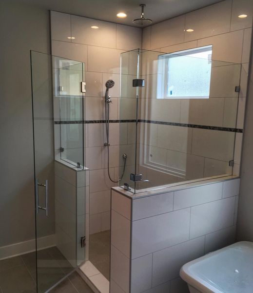 A modern bathroom with a glass-enclosed shower. Beige tiles, black accent lines, and a small window are visible.
