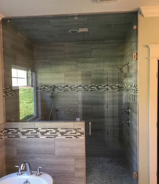 Glass shower enclosure with gray tile walls and a small window; a bathroom setting.