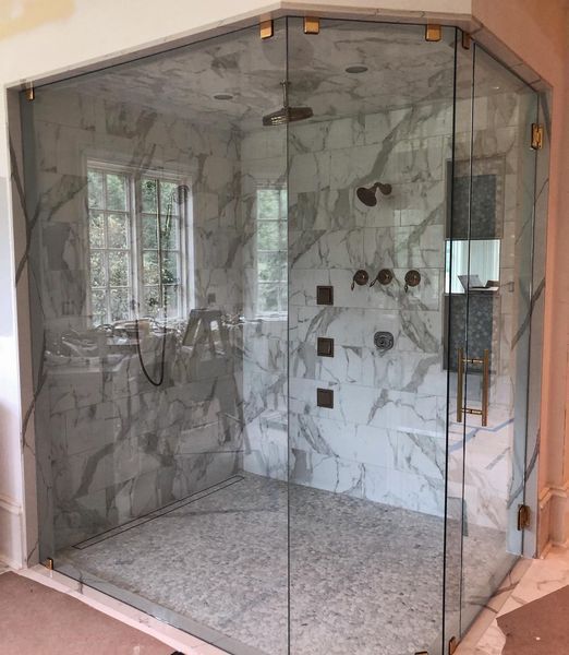 Corner shower with clear glass doors and marble tile walls; gold fixtures.