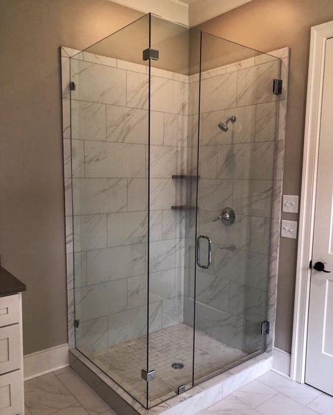 Corner shower enclosure with clear glass doors and white marble tile. Gray walls and a white door are also visible.