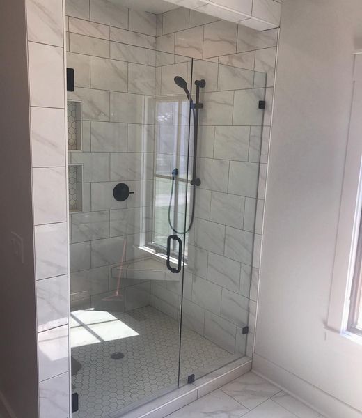 Modern shower enclosure with a glass door, black hardware, and white marble-look tile walls and floor.