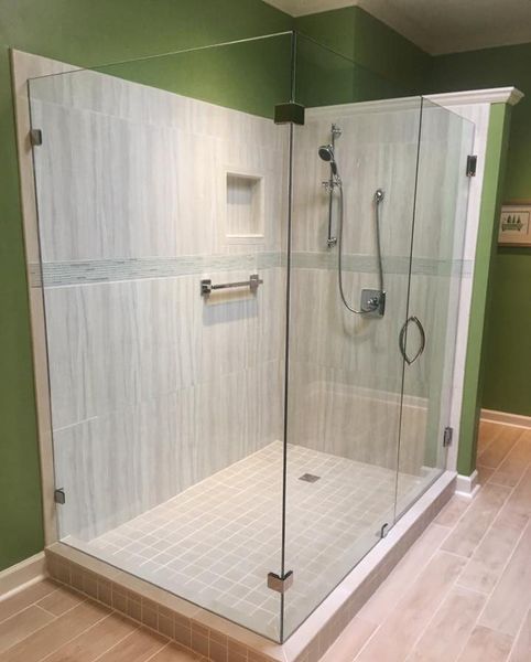 A modern glass shower with a tiled interior, chrome fixtures, and a built-in niche, set against green walls.