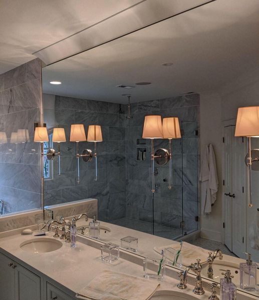 Bathroom with marble walls, large mirror, sconce lighting, and double sinks reflecting a shower stall.