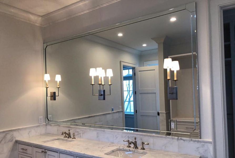 Large bathroom mirror above a white marble countertop with two sinks and gold sconce lighting.