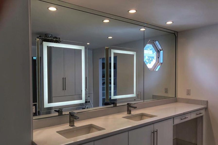Bathroom with long countertop, two sinks, large central mirror, two side mirrors with LED lights, and a round window.