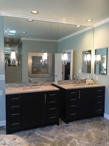 A modern bathroom with two black vanities, large mirror, and light blue walls. Each vanity has a square mirror and hanging light fixture.