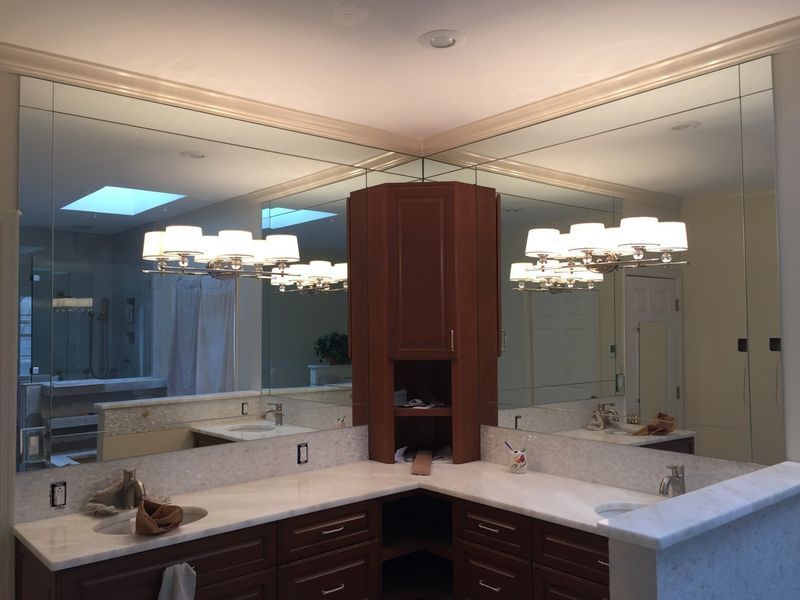 Bathroom with large mirrors on walls, reflecting the space. Brown cabinets, white countertops, and a skylight are visible.