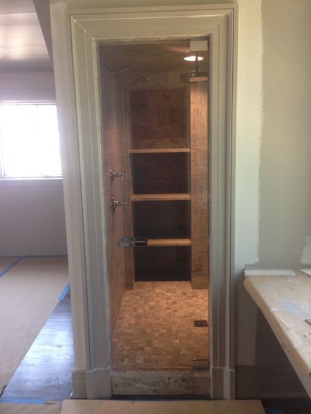 A walk-in shower under construction. Light-colored stone tile lines the walls and floor, with built-in shelves. The shower is framed in white.