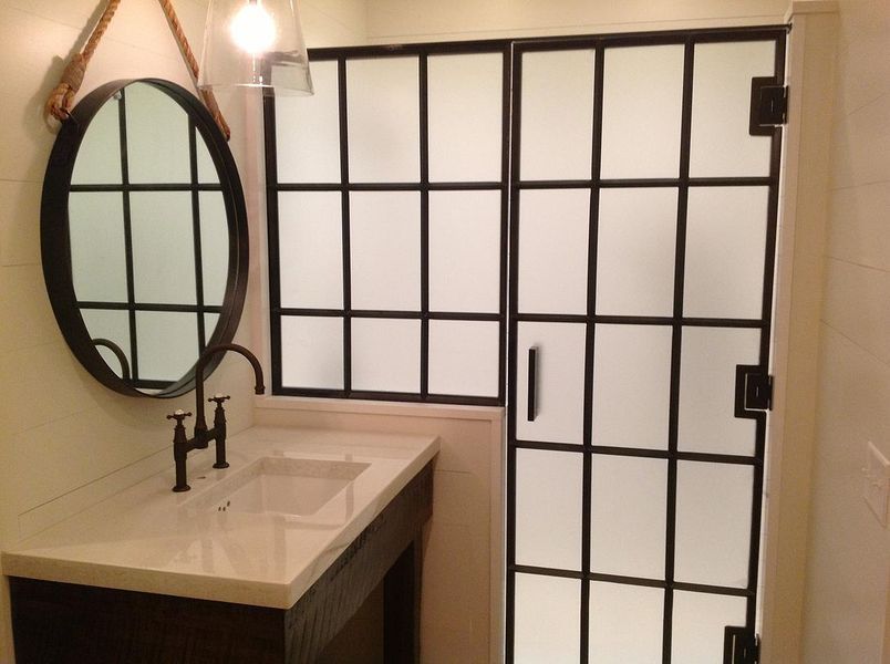 Bathroom with a dark-framed frosted glass shower and matching oval mirror. Black fixtures and a marble countertop are also present.
