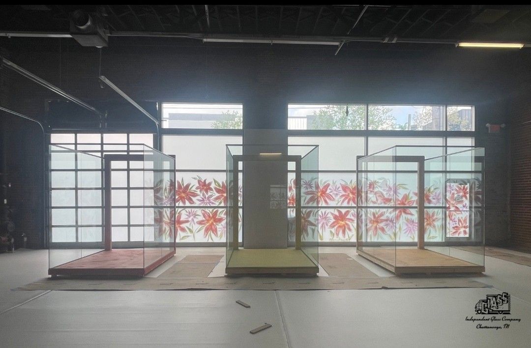 Three raised platforms with enclosed structures stand against a backdrop of windows with floral designs. The platforms are different colors.