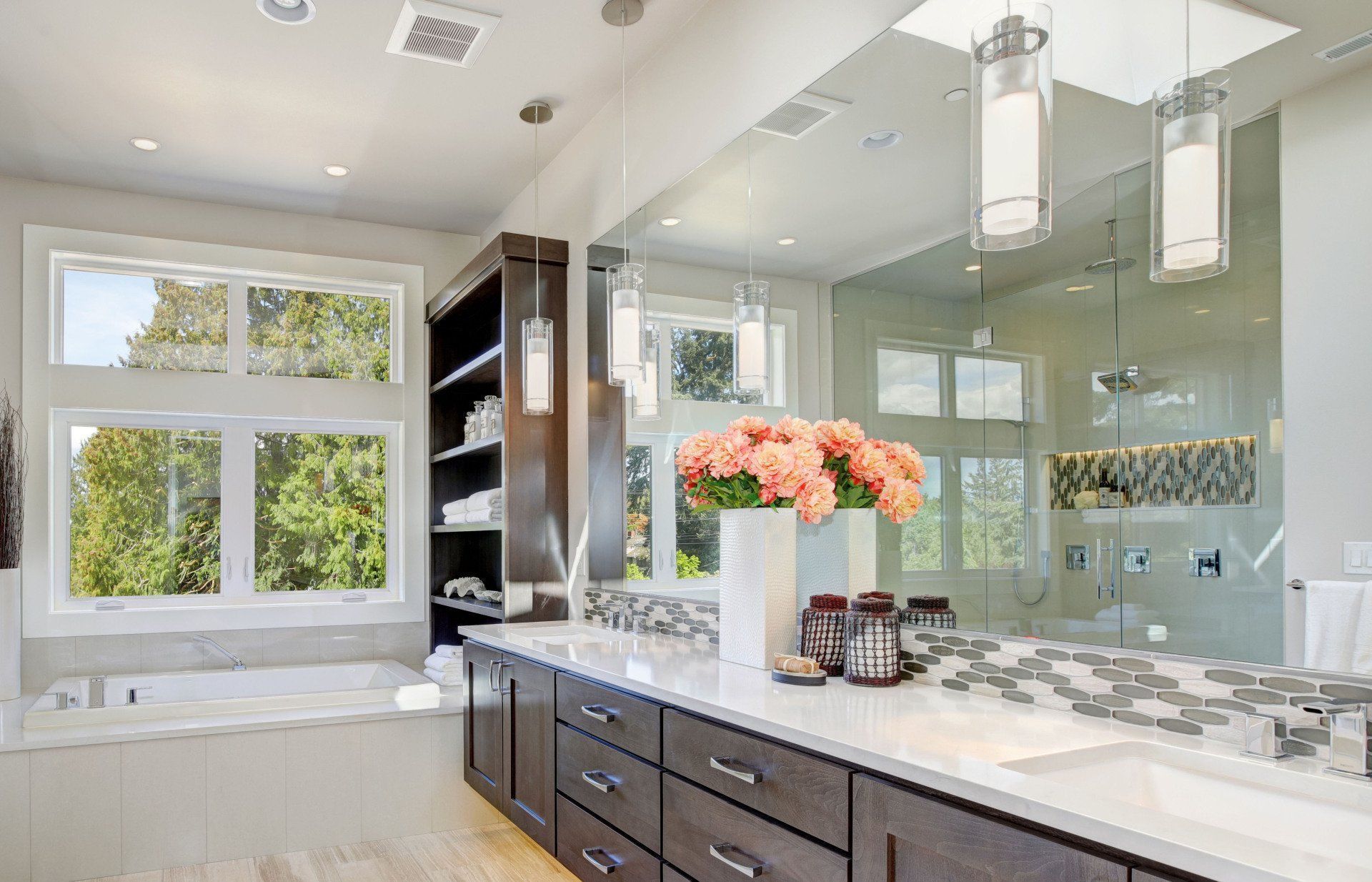 Bright, modern bathroom with a large vanity, soaking tub, and walk-in shower. Features a large mirror, built-in shelving, and a window overlooking greenery.
