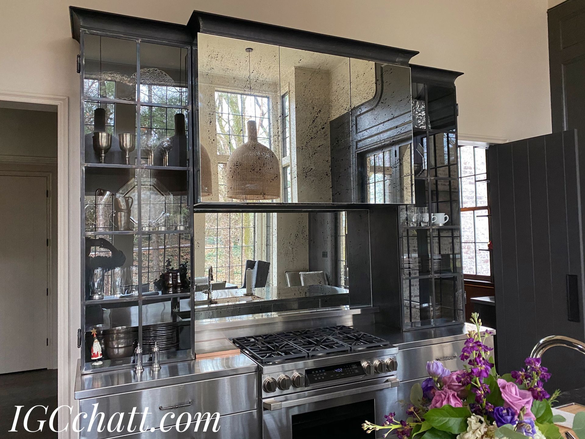 A modern kitchen with black cabinets, a stainless steel range, and a mirrored backsplash. A window is visible behind the stove.