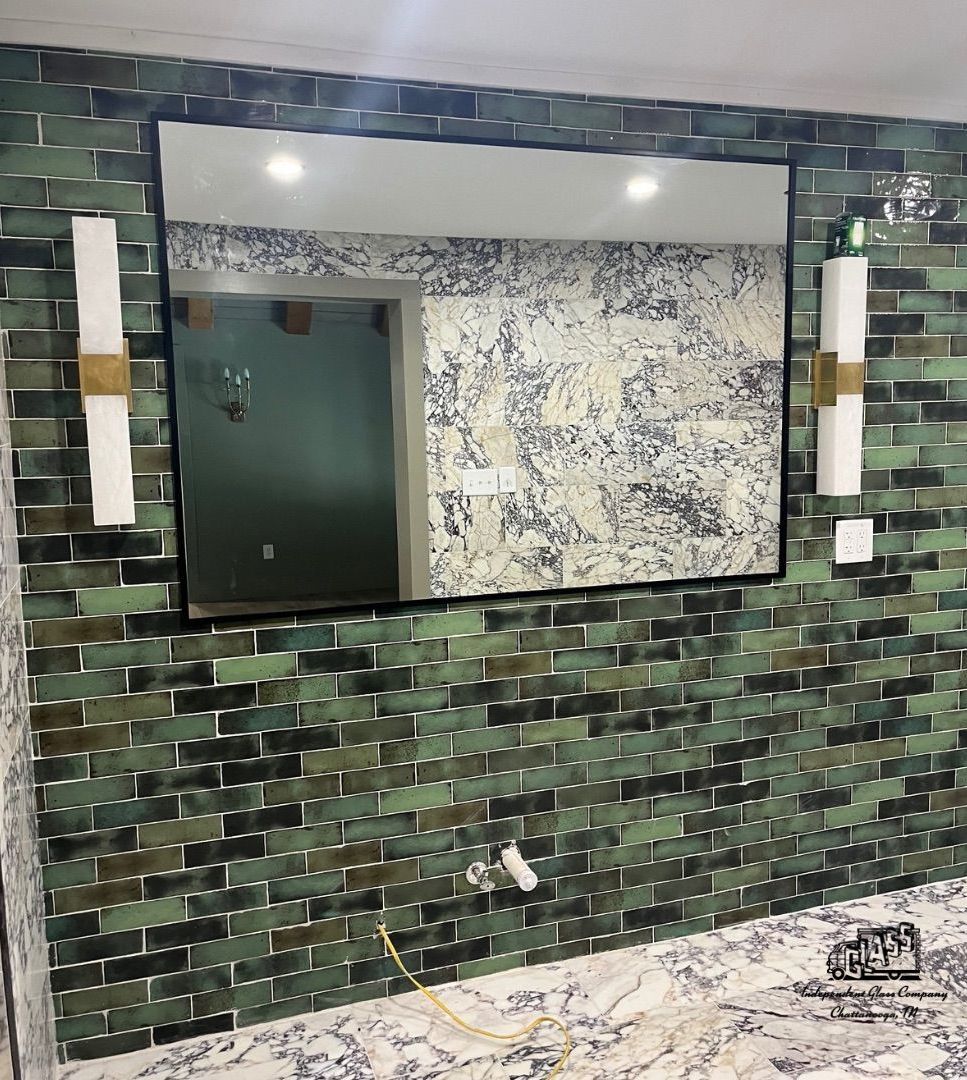 Bathroom with green mosaic tile backsplash, rectangular mirror, and sconces. The countertop is white marble with a small water faucet.