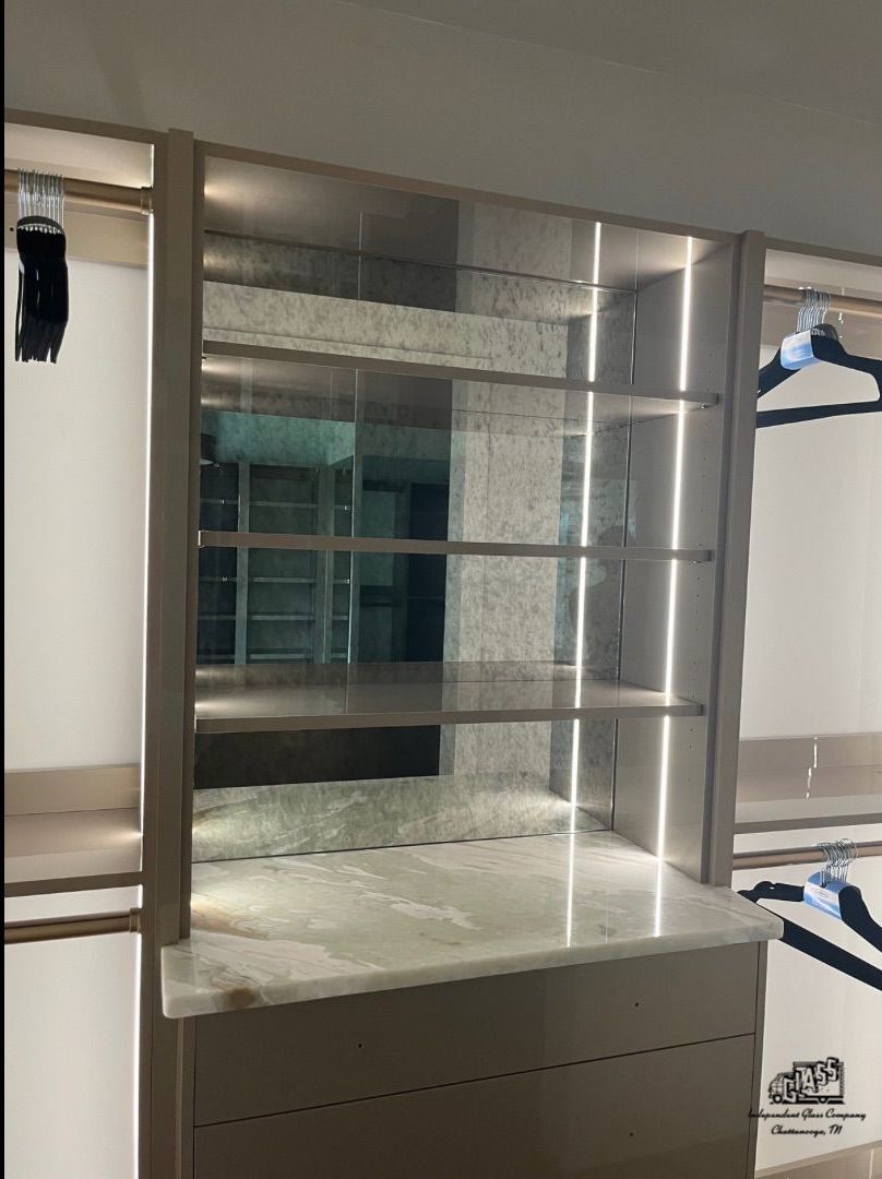 Built-in shelving unit with marble countertop and illuminated glass shelves. The unit is in a closet space.
