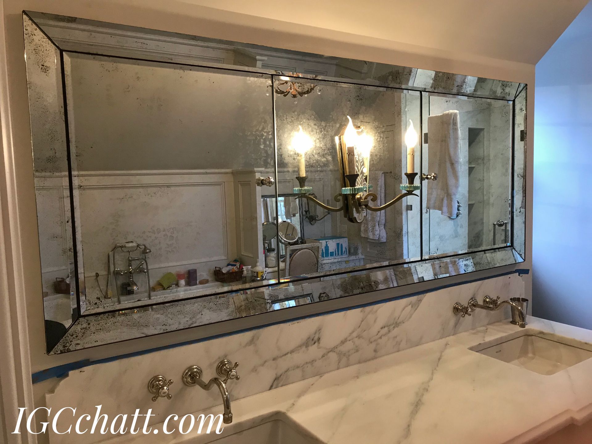 Bathroom with large, antique-style mirror above marble countertops with dual sinks and a chandelier. The mirror has an aged, speckled appearance.