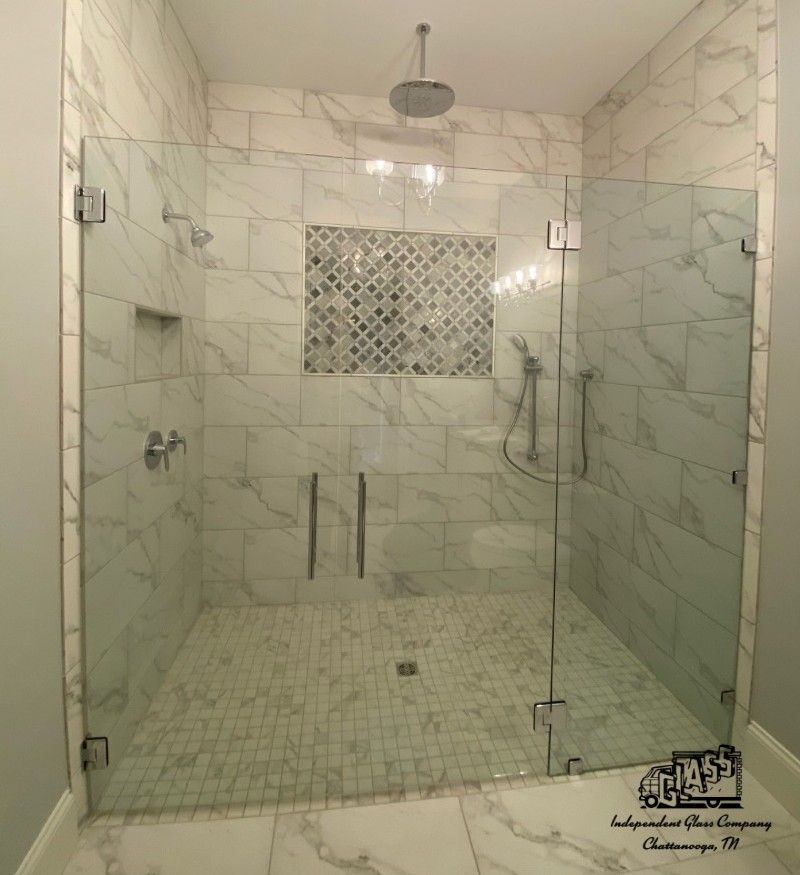 Modern shower with marble tile walls and frameless glass doors. Features a rain showerhead and handheld shower, and mosaic tile accent.