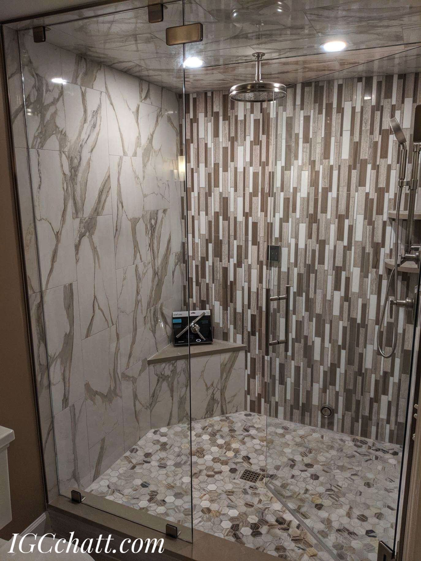 Shower with glass doors and pebble floor, featuring marble and textured tile walls.