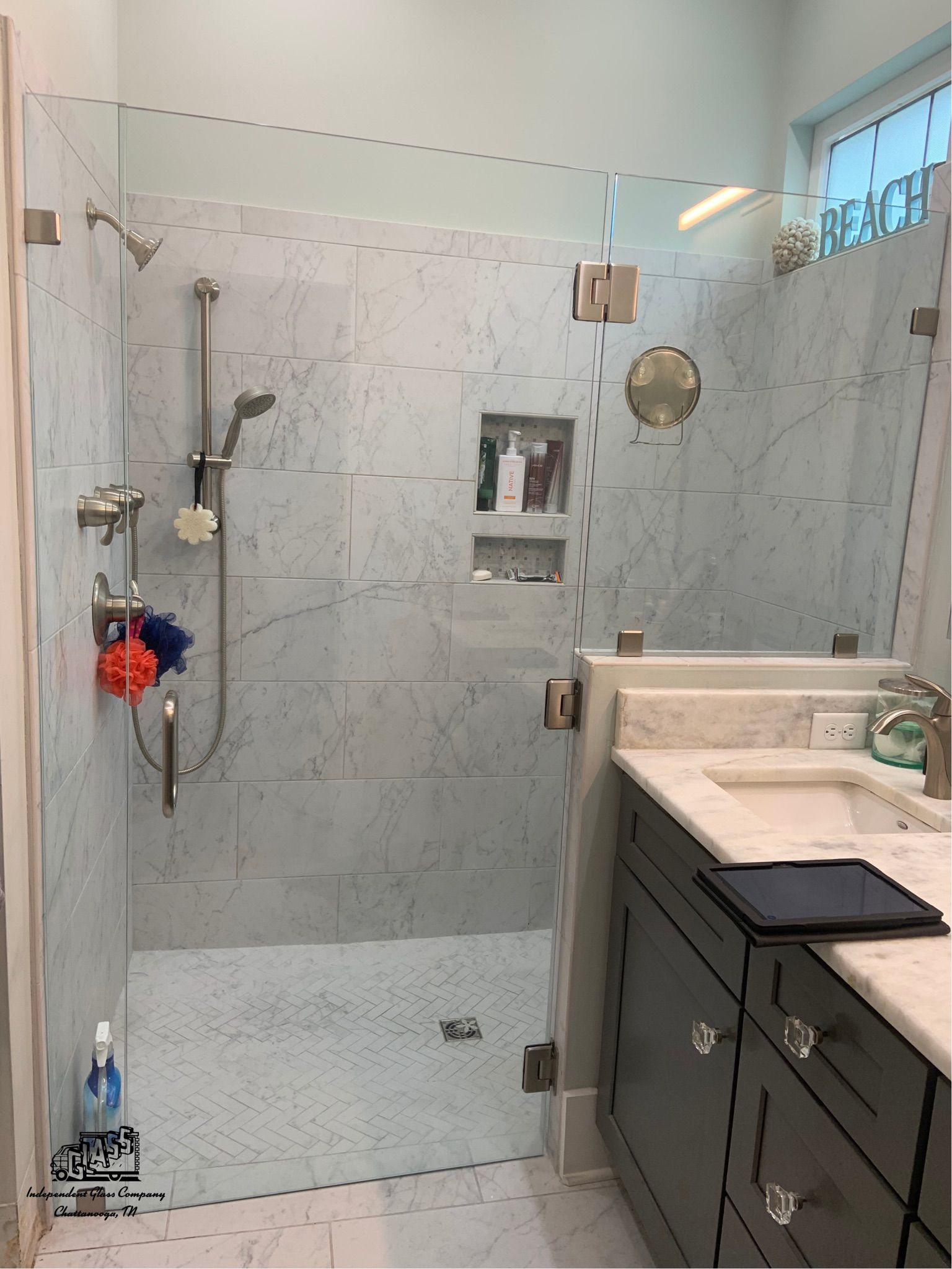 Glass-enclosed shower with marble tile walls, brushed nickel fixtures, and a vanity with a dark cabinet in a bathroom.