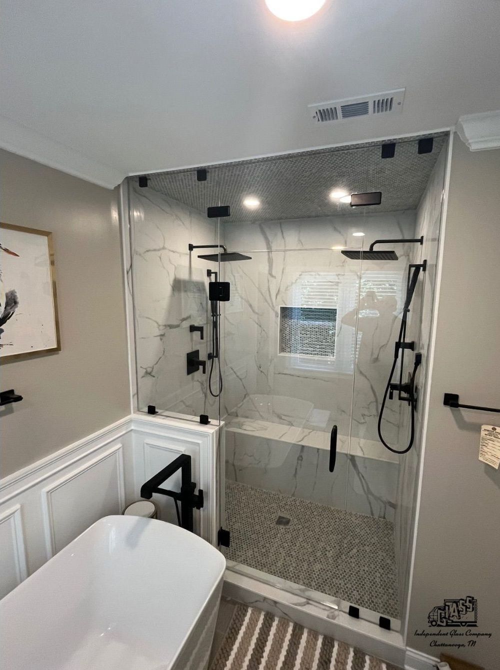 Modern bathroom with a large walk-in shower, marble-like tile, pebble floor, and a built-in bench. Black fixtures and glass enclosure.