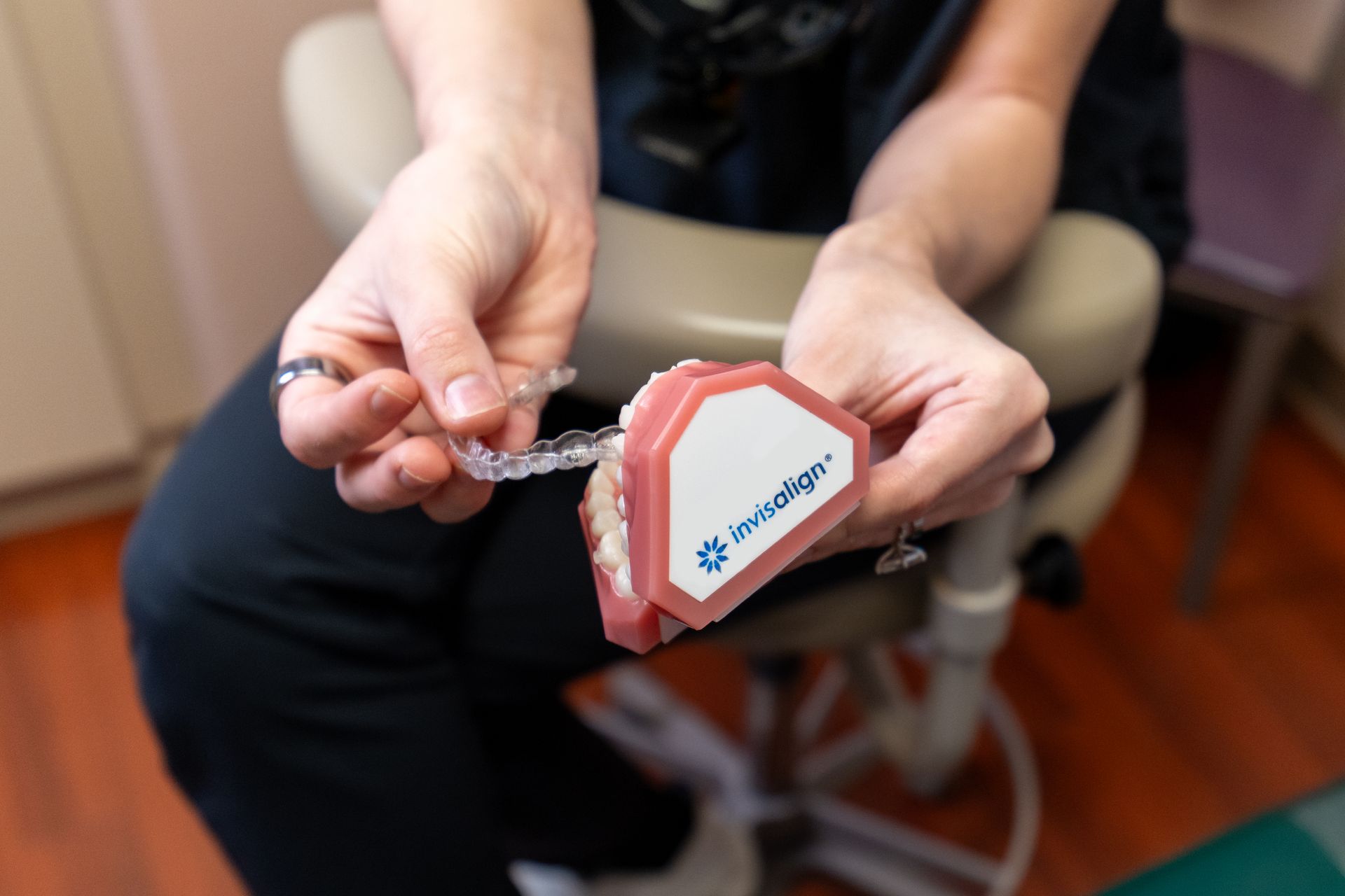 A person holds a dental model with an Invisalign clear aligner tray being placed over the teeth.