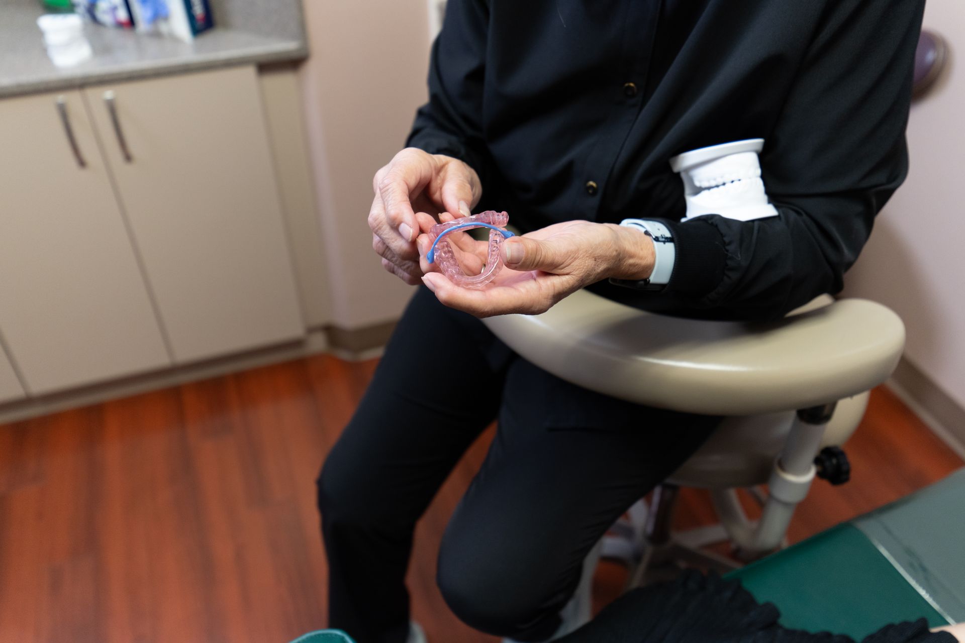 A dentist in a clinic setting holds a clear dental aligner tray.