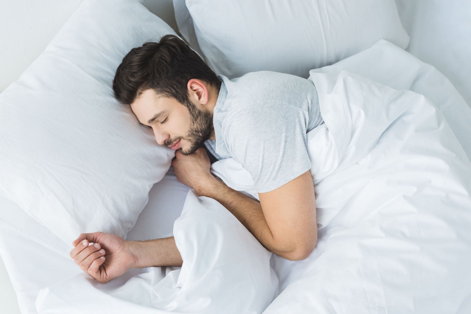 Man sleeping on white bed with a pillow, covered by a white blanket