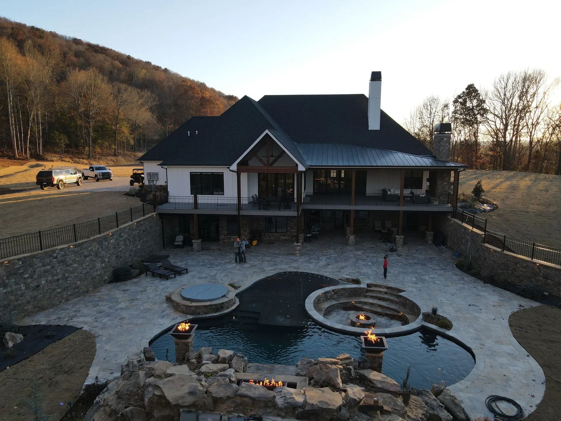 A multi-level home with a large backyard featuring a swimming pool, a stone fire pit, and a rocky landscaping waterfall.