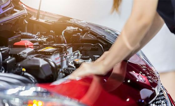 A man is looking under the hood of a red car.