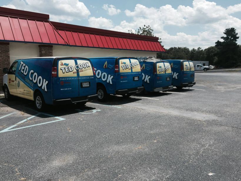 Four blue Ted Cook service vans parked outside a building with a red roof.
