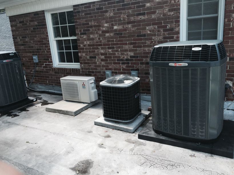 Air conditioning units on a rooftop near a brick building with windows.